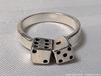 Close-up image of sterling silver ring with two dice design, showing details of pips and band from one angle.