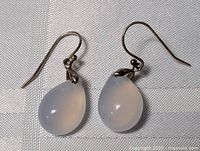 Close-up photo of a pair of sterling silver earrings with pear-shaped moonstone drops on white textile background.