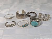 Seven vintage bracelets displayed on white fabric. Varied styles including cuffs, bangles, and linked bracelet.