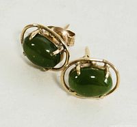 Close-up of green oval jade set in 10K yellow gold earrings showing stone color and gold framing.