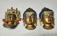 Photo showing the three hand painted metal Buddha heads arranged on a flat surface for viewing details, highlighting the painted facial features and crown decorations.