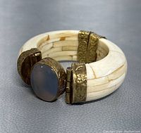 Side angle view of the wide cuff bracelet showing the segmented material with brownish veins and ornate brass hinge and gemstone centerpiece.