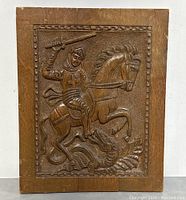 Full frontal image of the hand carved wood plaque showing the knight on horse and the dragon below with a textured background and border.