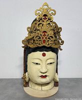Front view of the carved Balinese wooden head sculpture with gold headdress and facial details.