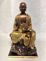 Front view showing the seated Kṣitigarbha figure with gold robes and bronze face, hands, and rock base.