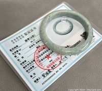 Top view of the jade bangle lying on a certification document with Chinese text and official stamps.