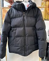 Front view of black Pajar winter jacket with zipper closed, showing hood and pockets