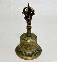 Brass Tibetan Buddhist prayer bell showing detailed embossed patterns on bell body and ornate Vajra handle.