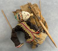 Handcrafted Indonesian stick puppet laid flat showing full body, fabric garments, and wooden sticks used for control.