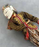 Close-up of the puppet laid on gray surface, showing detailed face and upper body with striped costume and gold lace trim.