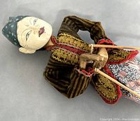 Close-up photo of the puppet's face, headgear, and detailed embroidery on clothing. Shows painted facial details and piece's craftsmanship.