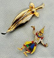 Front view of Siam sterling silver swirl brooch and colorful enamel dancer brooch displayed on gray background.