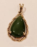Front view of pendant showing teardrop green jade cabochon set in 14K yellow gold with branch-like prongs.