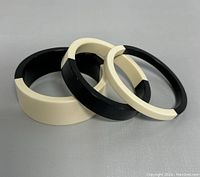 Three black and cream lucite bangles shown stacked and arranged on grey background with visible light scratches and minor wear.