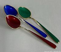 Three sterling silver teaspoons showing guilloche enamel in blue, red, and green on front side, arranged at an angle.