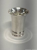 Front view of flared 830 silver christening cup showing smooth polished surface, flared top and decorative bands near base.