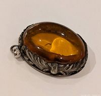 Close-up front view of the pendant showing the oval amber stone and silver detailed setting with floral and bird designs.