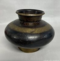 Front view of the round, bulbous old brass drinking water vessel with engravings and patina.