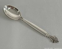 4.5-inch sterling silver spoon with decorative scroll and geometric handle design, polished finish, minor wear visible.