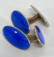 Close-up photo of two oval-shaped blue guilloche enamel cufflinks with sterling silver framing and connecting bar.
