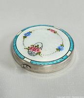 Closed view of the round sterling silver compact showing the enamel floral design on top.