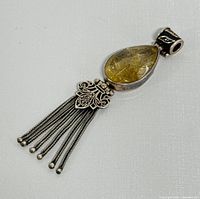 Overall view of vintage sterling silver pendant with rutilated quartz and tassel detail on white background.