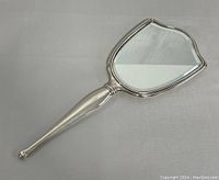 Full view of the vintage handheld mirror showing its shield-shaped frame and tapered handle with a polished silver finish.