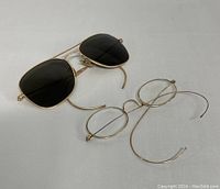 Both pairs of vintage eyewear displayed on a white surface showing sunglasses and oval eyeglasses.