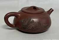 Angle view of the handmade Chinese clay teapot showing engraved landscape detail and rounded handle.