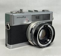 Front angle view showing Minolta 7S logo, lens with CLC marking and textured black and silver body.