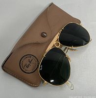 Ray-Ban aviator sunglasses resting on original brown leather-like case showing the front side and branding.