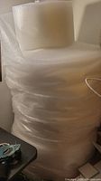 Stack of large clear bubble wrap rolls against a wall