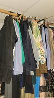 Photo showing a side view of assorted hanging clothing on a wooden rod including a dark brown suede jacket and light blue shirt.