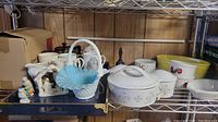 Shelf with assorted ceramic and glass items including a blue glass basket with white handle, small ceramic decorative pieces, and white casserole dish with a lid.