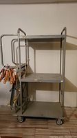 Front view of the large metal shelf cart showing three metal shelves, handle, and ladder attachment.