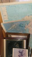 Several framed maps and various framed artwork stacked against a wall