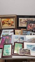 Mixed lot artworks shown against white background including framed child painting, historical print, postcards, landscapes, and album cover art