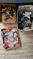 Three boxes showing multiple vintage toys including wrestling figures, packaged toy accessories, and additional vintage toys such as a Star Wars R2-D2 figure.
