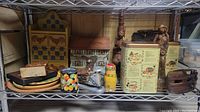 Shelf with wooden carved statues, vintage tins, and other collectibles including carved wood and metal items.