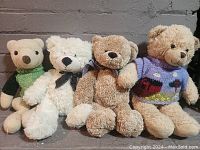 Four teddy bears arranged sitting on a brick ledge, showing various colors and accessories.