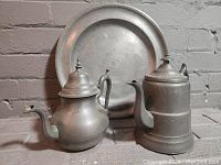 Full view of the charger plate, coffee pot, and teapot arranged together against a brick wall.