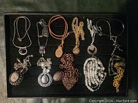 View of all eleven costume necklaces laid flat on black background, showing diversity in design and materials.