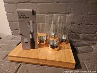 Photo showing bamboo cutting board with four beer glasses with gold-colored bases and boxed wine aerator.