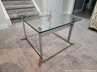 Full view of the mid-century modern glass topped coffee table on carpeted floor, showing square glass top and chrome metal frame base.