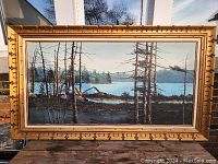 Full view of large original oil painting in ornate gold frame depicting a lakeside landscape with trees and rocky shoreline under a soft sky.