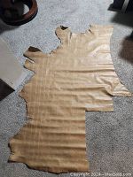 Full view of the partial half hide of light tan leather laid out flat on carpeted floor, showing overall shape and size.