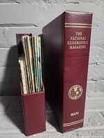 Photo of vintage National Geographic branded binders in burgundy color, one standing upright and one open holding supplements.