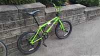 Full side view of green DK Rise BMX bike leaning against stone wall.