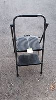 Front view of the black folding 2-step ladder showing non-slip textured steps and padded handle.
