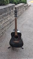 Front view of black Yamaha acoustic guitar on stand outdoors by stone retaining wall.